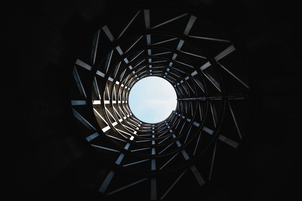 Looking up through a spiral of steel beams toward open sky